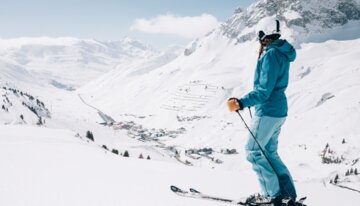 © Daniel Zangerl, Lech Zürs Tourismus A female skier in blue ski clothing stands on the slope and looks into the distance. | © Daniel Zangerl, Lech Zürs Tourismus