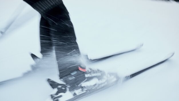 Close-up of lower legs and skis in motion with snow spraying up; visible “Salomon” brand on ski boot. | © INTERSPORT International Corporation GmbH