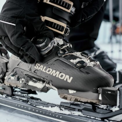 Close-up of a hand wearing a ski glove adjusting a snow-covered Salomon ski boot buckle on a tied ski binding. | © INTERSPORT International Corporation GmbH