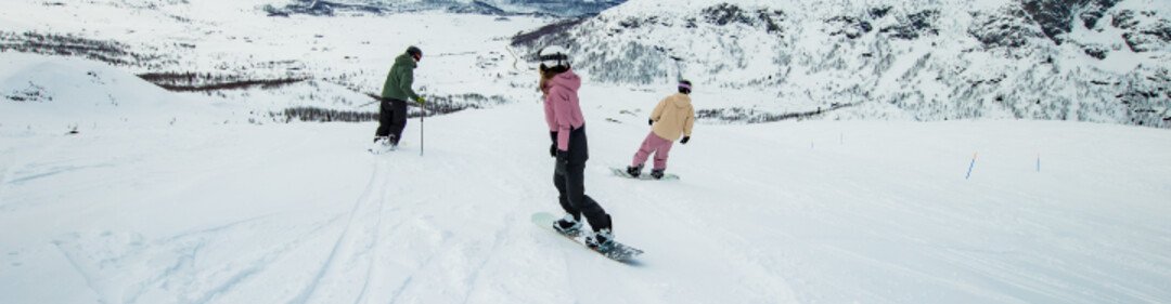 Two snowboarders and a skier are skiing down a snow-covered mountain.