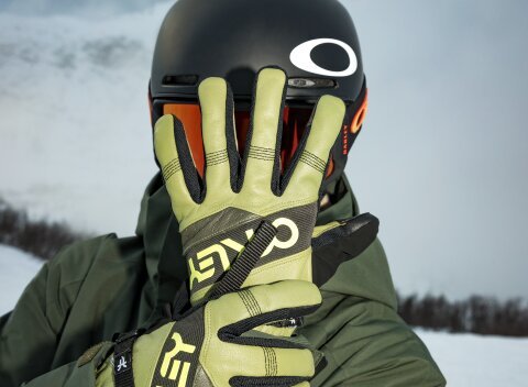 Man in a green ski suit with matching Oakley ski goggles and Oakley ski gloves holds his left hand open in front of his face while his right hand grasps his left wrist.  | © 30.09.2026
