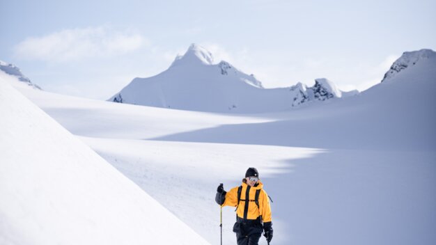 Ski tourer in a yellow jacket with ski poles in a wide, snowy mountain landscape in front of snow-covered peaks. | © INTERSPORT International Corporation GmbH
