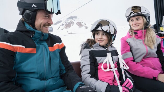 Familie fährt Ski-Lift, alle tragen Helme und Skibrillen. | © IIC/McKINLEY