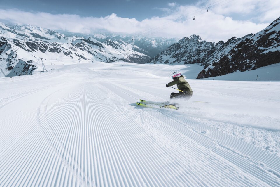 Skier on a groomed slope in a snowy mountain landscape.