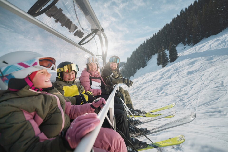 © INTERSPORT International Corporation GmbH Family riding a ski lift on a sunny day. | © INTERSPORT International Corporation GmbH