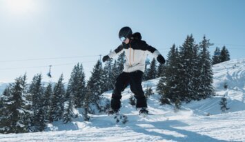 Snowboarder springt in der Luft vor verschneitem Hintergrund. | © INTERSPORT International Corporation GmbH
