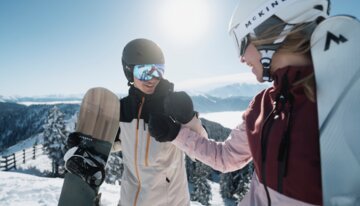 Zwei Snowboarder geben sich die Hand im Schnee. | © INTERSPORT International Corporation GmbH