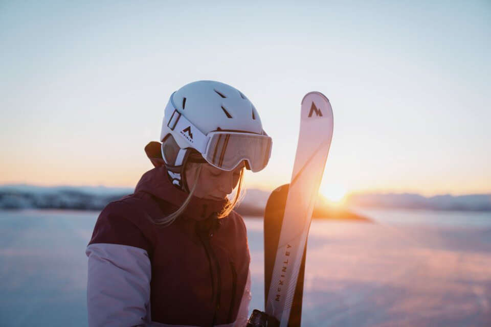 © INTERSPORT International Corporation GmbH Skier wearing a helmet and holding skis at sunset | © INTERSPORT International Corporation GmbH