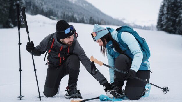 Zwei Personen befestigen Schneeschuhe im Schnee. | © INTERSPORT International Corporation GmbH