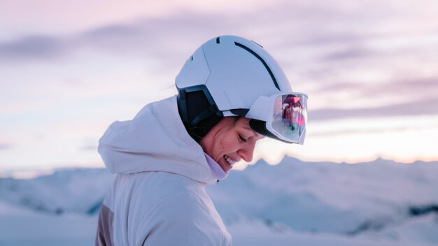 Woman with ski helmet and goggles smiling in the snow.