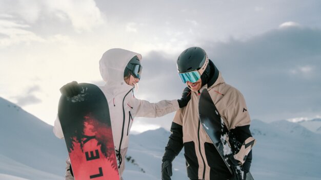 Zwei Snowboarder stehen mit Snowboards in einer verschneiten Landschaft.