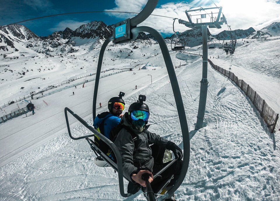 Two skiers on a chairlift with snowy mountain landscape in the background.