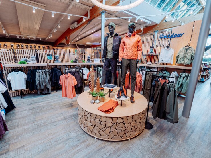 Retail area of an INTERSPORT Rent shop with outdoor apparel, display tables and clothing collections on racks