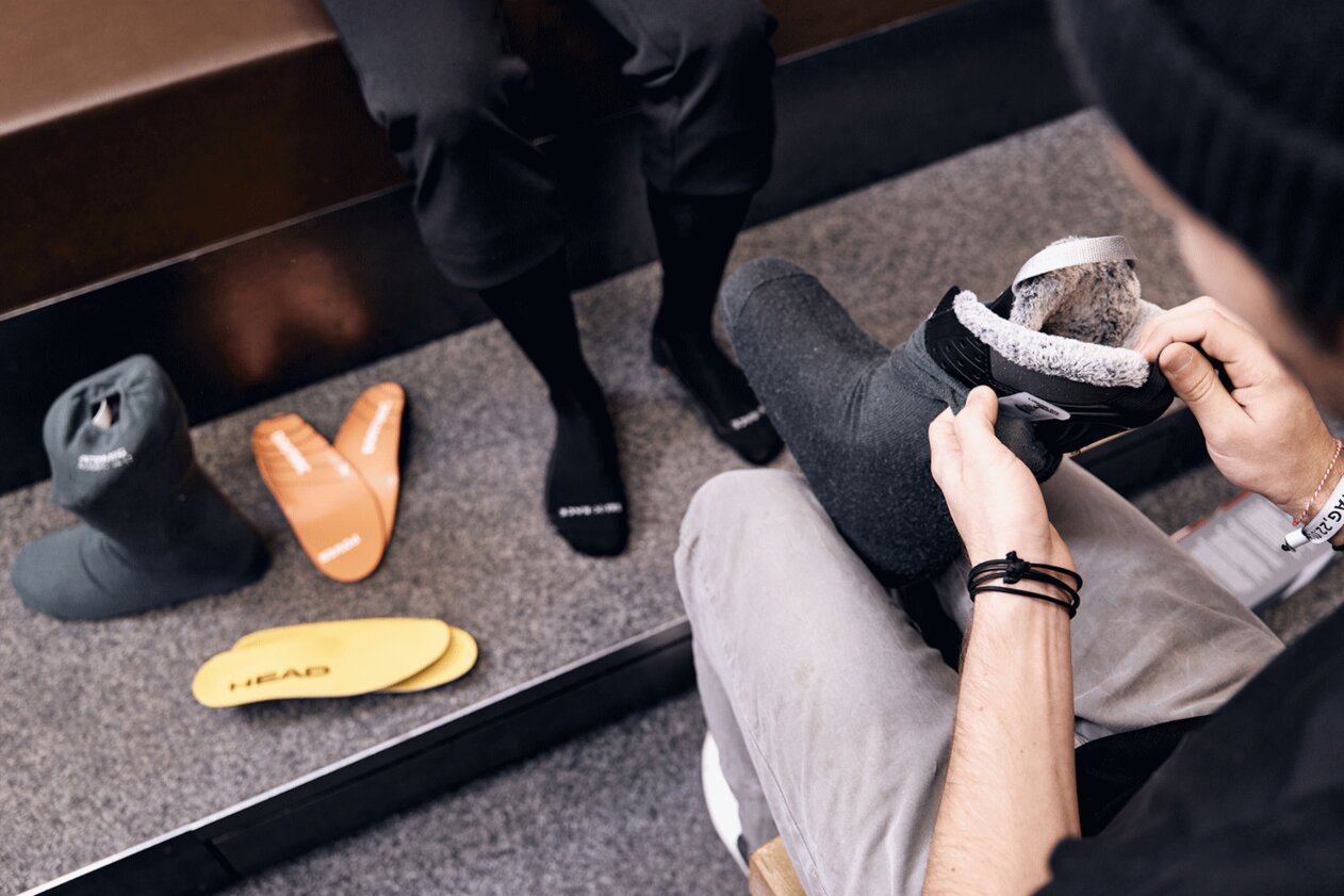Person fitting ski boot, with insoles and sock liners beside