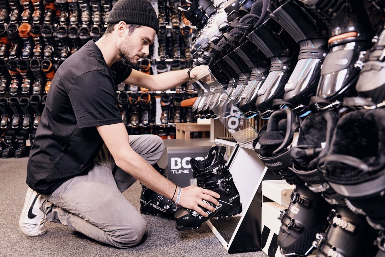 Man kneeling in front of ski boot display, examining a ski boot.
