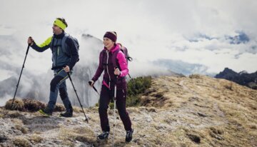 Zwei Wanderer mit Stöcken auf einem Bergpfad.