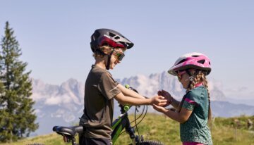 Zwei Kinder mit Fahrrädern tauschen etwas in ihren Händen.