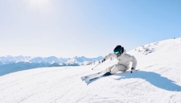Skier in white carving down a sunny snowy slope.